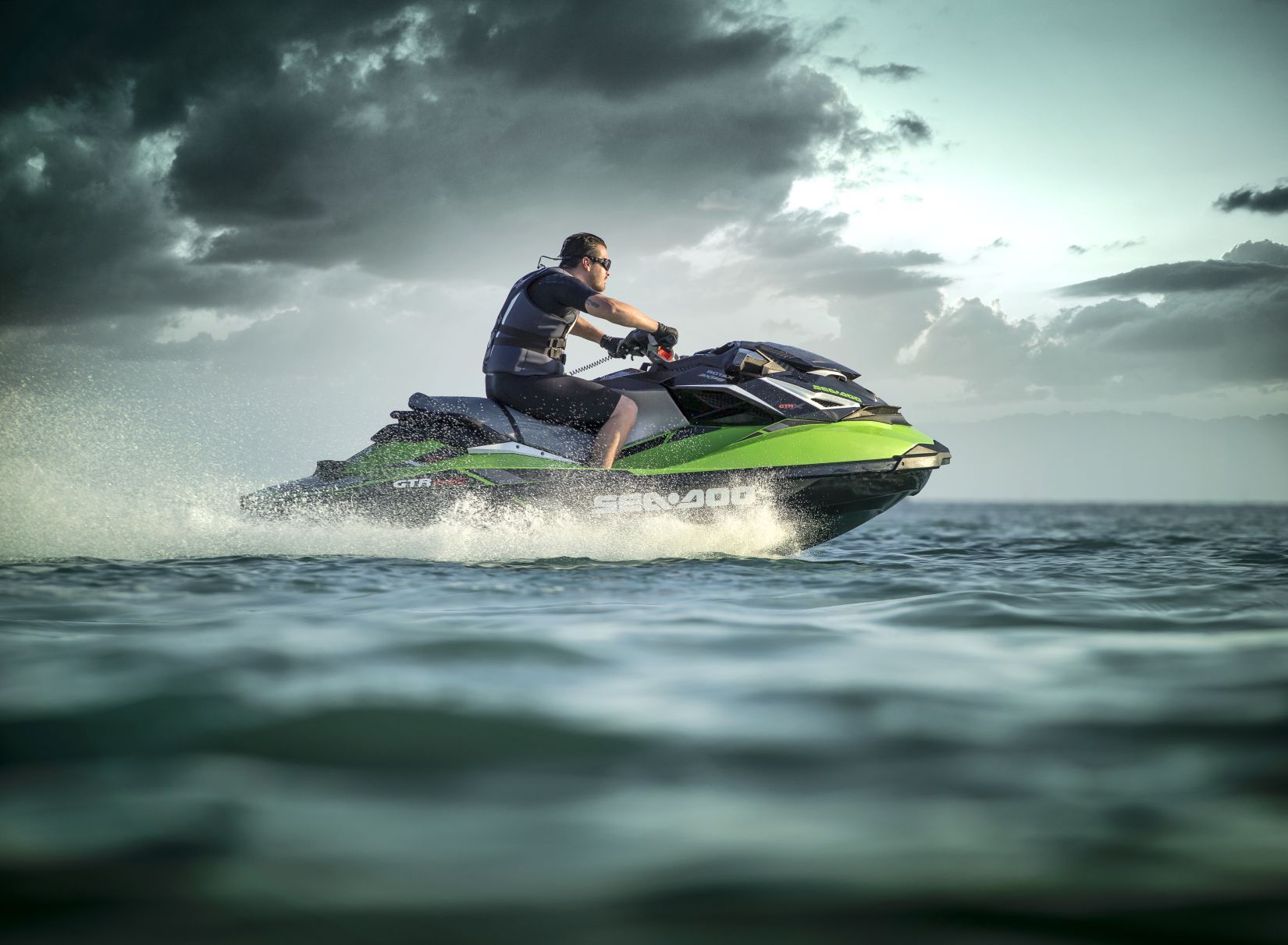 A rider on a green Sea-Doo GTR-X personal watercraft at speed on open water